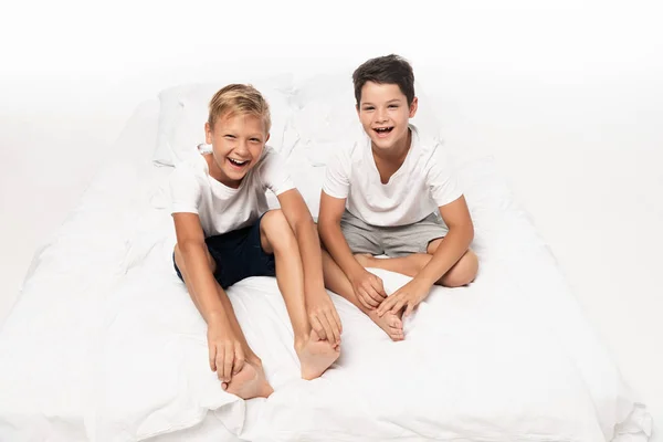 Two happy brothers sitting on bed and smiling at camera on white background — Stock Photo