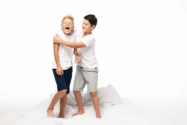 Cheerful boy jokingly pulling hair of screaming brother isolated on white — Stock Photo