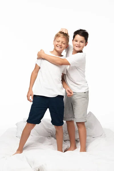 Alegre chico abrazando hermano y bromeando tirando de su pelo mientras aislado en blanco - foto de stock