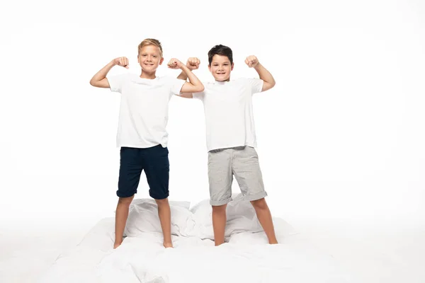 Dos hermanos imitando culturistas de pie en la cama aislado en blanco - foto de stock