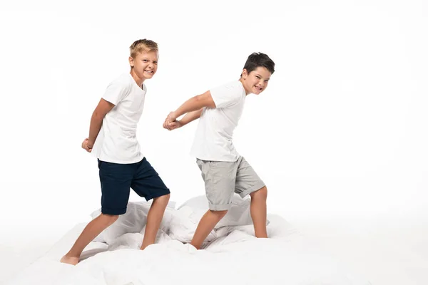 Dois irmãos alegres imitando fisiculturistas enquanto em pé na cama isolado no branco — Fotografia de Stock