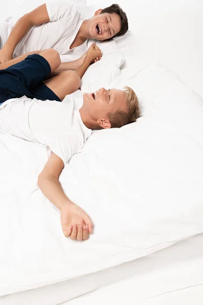 Deux frères heureux riant tout en étant couché sur la literie sur fond blanc — Photo de stock