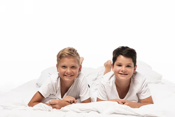 Two happy brothers lying on bed and smiling at camera isolated on white — Stock Photo