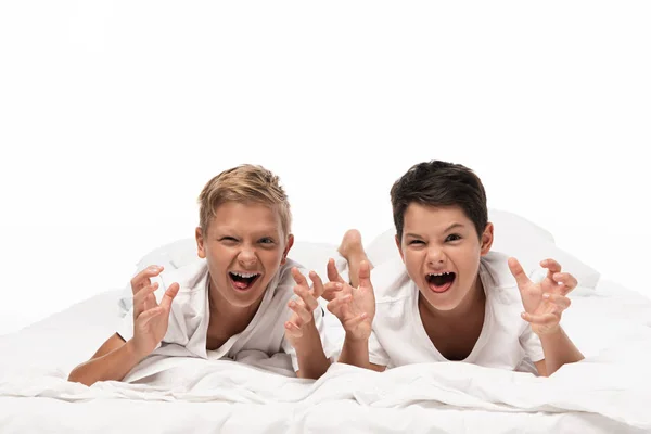 Two brothers grimacing and showing frightening gestures while lying on bed isolated on white — Stock Photo