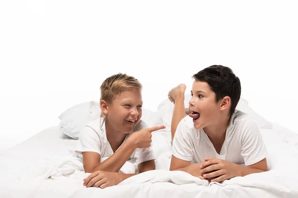 Alegre chico apuntando con el dedo a hermano sobresaliendo lengua aislada en blanco - foto de stock