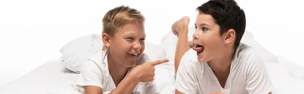 Panoramic shot of cheerful boy pointing with finger at brother sticking out tongue isolated on white — Stock Photo