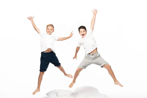 Dois irmãos excitados levitando sobre a cama e olhando para a câmera isolada no branco — Fotografia de Stock