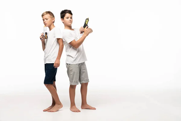 Two brothers standing back to back, holding toy guns and looking at camera on white background — Stock Photo