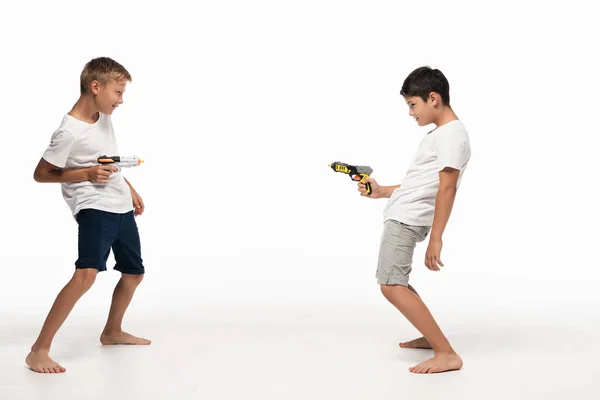 Two brothers aiming at each other with toy guns on white background — Stock Photo