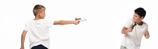 Panoramic shot of boy aiming with toy gun at scared brother isolated on white — Stock Photo