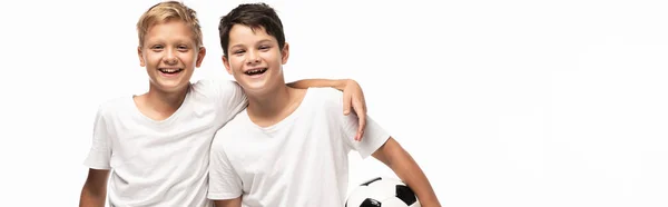 Панорамний знімок щасливого хлопчика обіймає брата, тримає футбольний м'яч ізольовано на білому — стокове фото