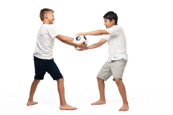 Непослушный мальчик забирает футбольный мяч у брата на белом фоне — стоковое фото