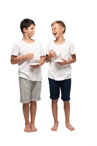 Alegres hermanos mirándose mientras sostienen tazas de café sobre fondo blanco - foto de stock