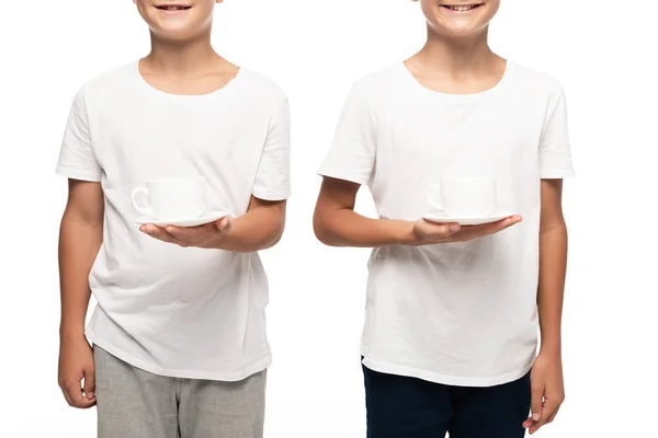 Vista recortada de dos hermanos sonrientes sosteniendo tazas de café aisladas en blanco - foto de stock