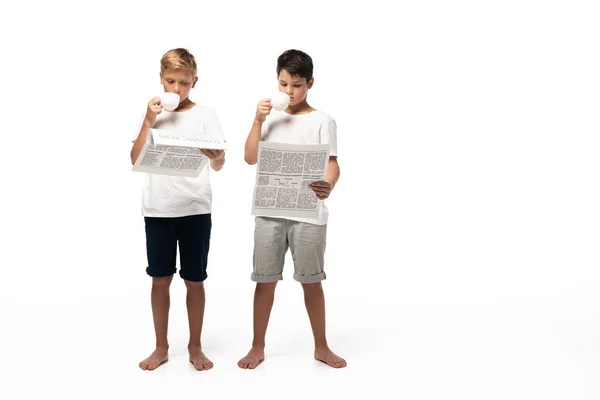 Two brothers reading newspapers and drinking coffee on white background — Stock Photo