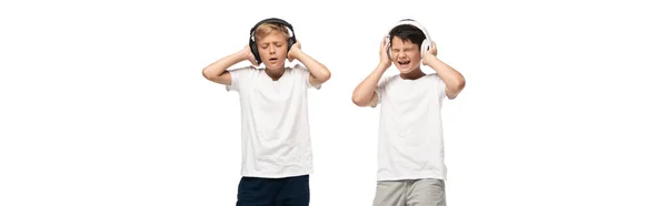 Panoramic shot of two excited brothers holding hands on headphones while listening music isolated on white — Stock Photo