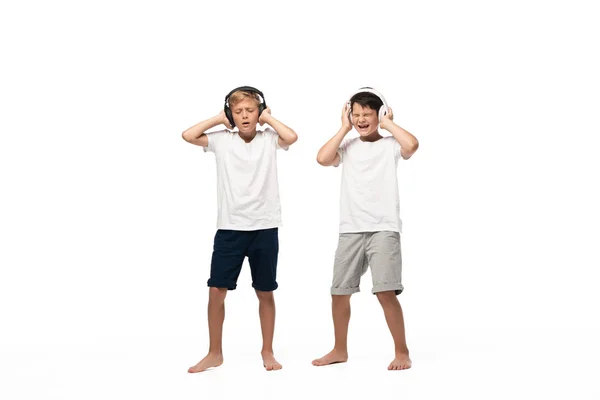 Deux frères excités tenant la main sur des écouteurs tout en écoutant de la musique isolée sur blanc — Photo de stock