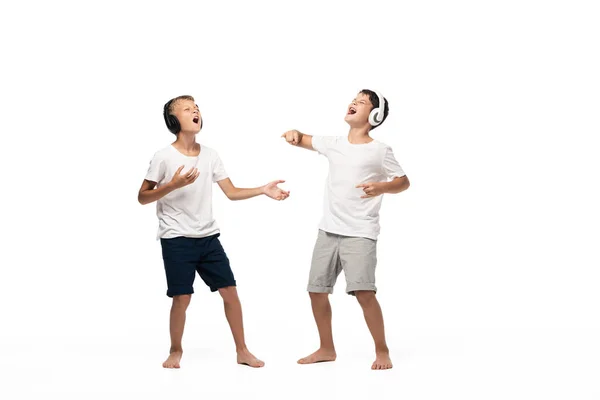 Two excited brothers singing with closed eyes while listening music in headphones — Stock Photo
