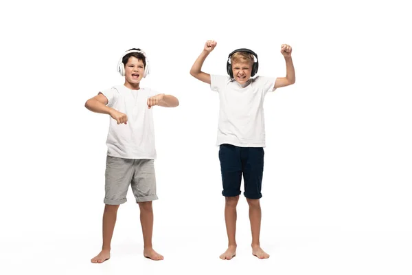 Dos hermanos alegres escuchando música en auriculares y bailando sobre fondo blanco - foto de stock