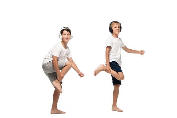 Dos hermanos alegres mirando a la cámara y bailando en auriculares sobre fondo blanco - foto de stock