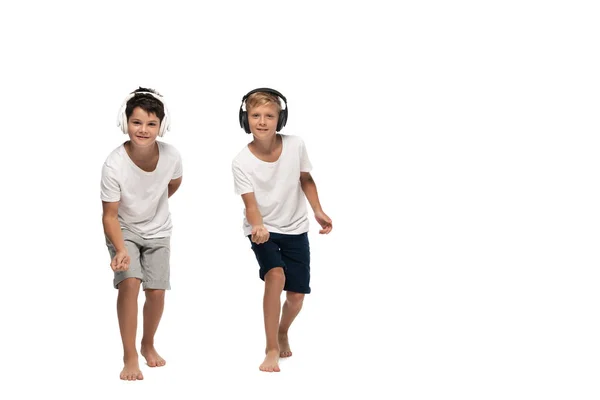Dois irmãos olhando para a câmera e dançando enquanto ouvem música em fones de ouvido no fundo branco — Fotografia de Stock