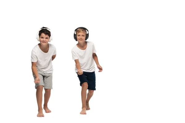 Two brothers looking at camera and dancing while listening music in headphones on white background — Stock Photo