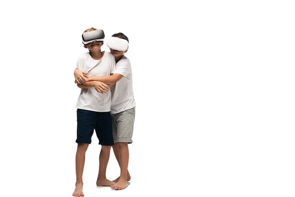 Junge umarmt lächelnden Bruder, während mit VR-Headsets zusammen auf weißem Hintergrund — Stockfoto