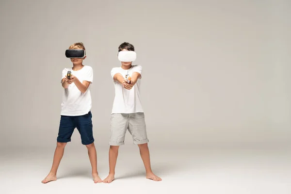 Two brothers in vr headsets aiming with toy guns at camera on grey background — Stock Photo