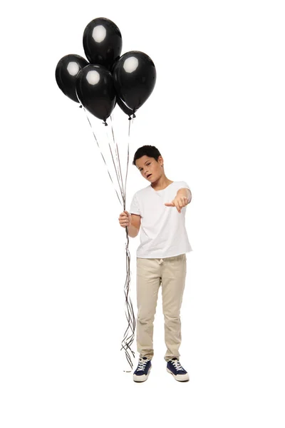 Chico serio apuntando con la mano a la cámara mientras sostiene globos negros sobre fondo blanco - foto de stock