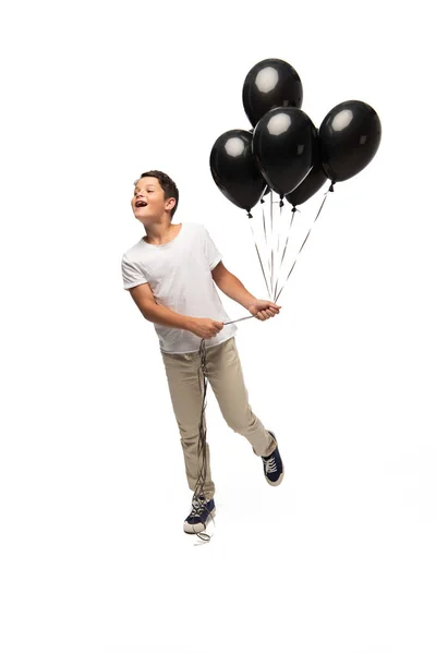 Aufgeregter Junge schaut weg, während er schwarze Luftballons auf weißem Hintergrund hält — Stockfoto