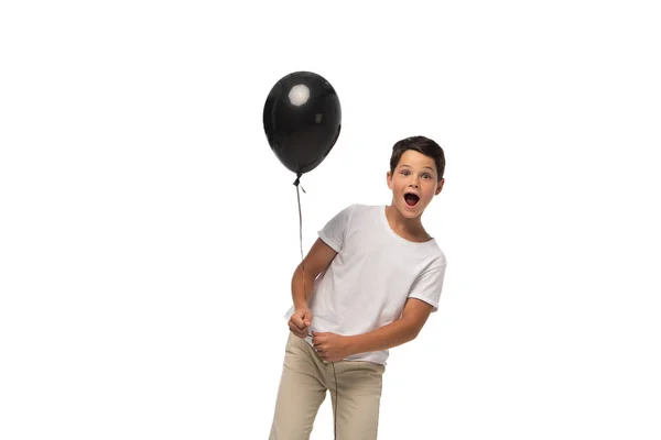 Menino surpreso olhando para a câmera enquanto segurando balão preto isolado no branco — Fotografia de Stock