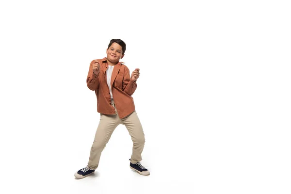 Fröhlicher Junge tanzt, während er in die Kamera auf weißem Hintergrund blickt — Stockfoto
