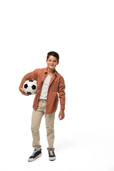 Menino alegre segurando bola de futebol e olhando para a câmera no fundo branco — Fotografia de Stock