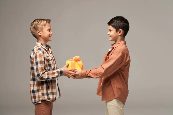 Two happy brothers holding yellow gift box while looking at each other isolated on grey — Stock Photo