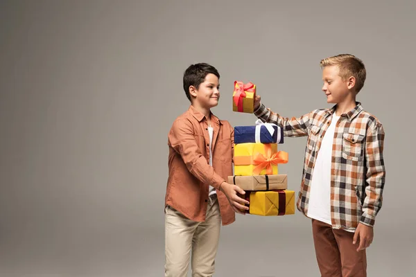 Felice ragazzo tenendo pila di scatole regalo multicolore vicino allegro fratello isolato su grigio — Foto stock
