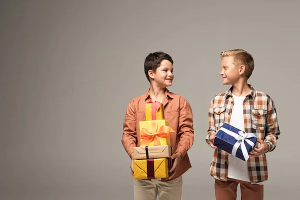 Two happy brothers holding multicolored gift boxes and looking at each other isolated on grey — Stock Photo