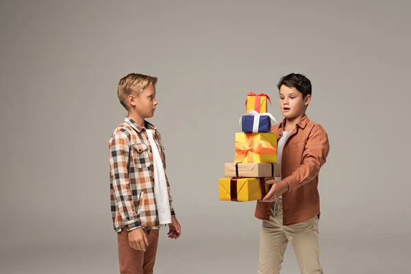 Überraschter Junge hält Stapel bunter Geschenkboxen in der Nähe von erstaunten Bruder isoliert auf grau — Stockfoto