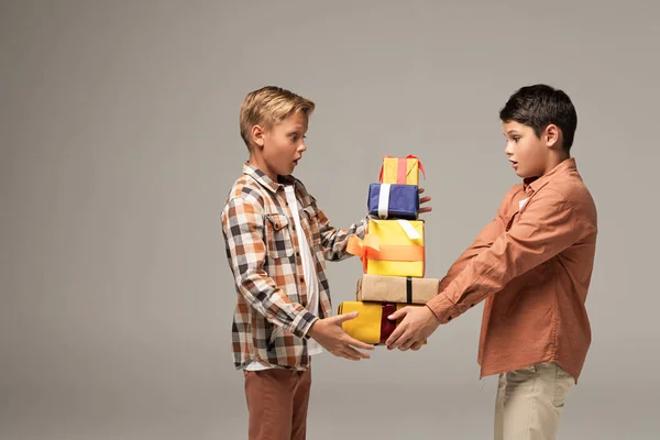 Два здивовані брати тримають стос різнокольорових подарункових коробок ізольовані на сірому — стокове фото