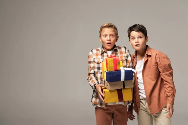 Два удивленных брата показывают стопку подарочных коробок, изолированных на сером — стоковое фото