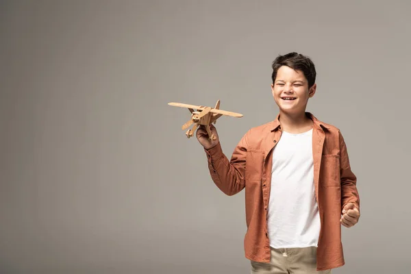 Menino feliz segurando avião de brinquedo de madeira e mostrando sim gesto isolado no cinza — Fotografia de Stock