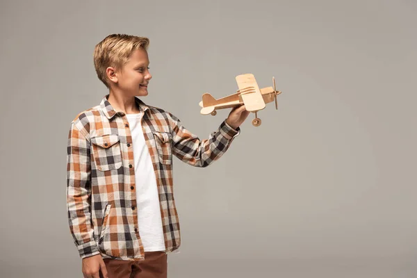 Smiling boy holding wooden toy plane isolated on grey — Stock Photo