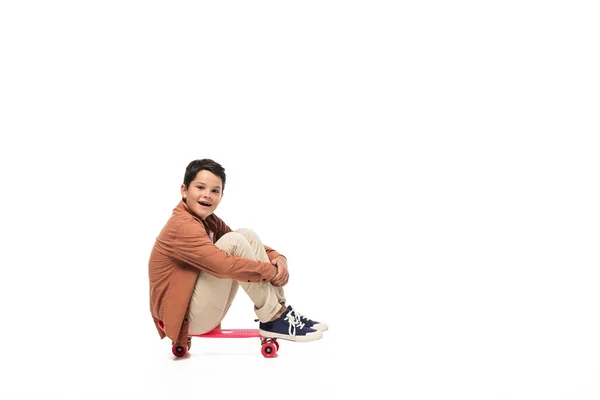 Smiling boy sitting on penny board and looking at camera on white background — Stock Photo