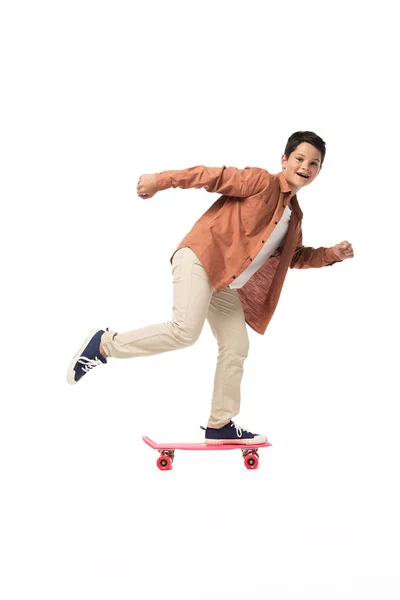 Menino alegre montando penny board enquanto olha para a câmera no fundo branco — Fotografia de Stock