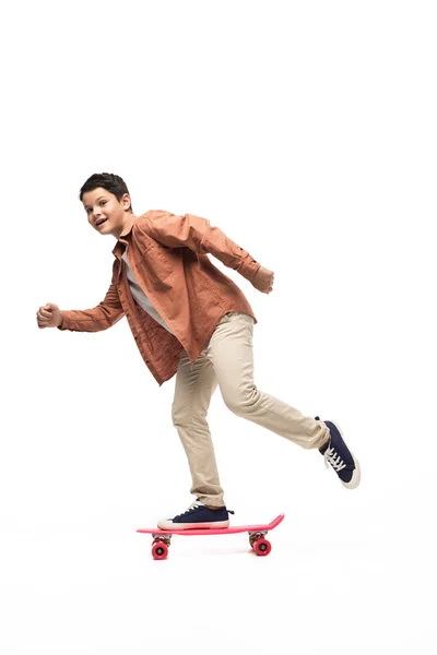 Aufgeregter Junge reitet Penny Board, während er in die Kamera auf weißem Hintergrund schaut — Stockfoto