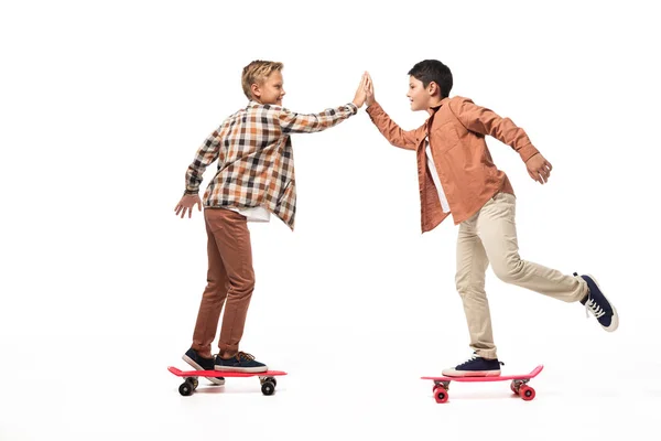 Fröhliche Brüder, die High Five geben, während sie Penny Boards auf weißem Hintergrund reiten — Stockfoto