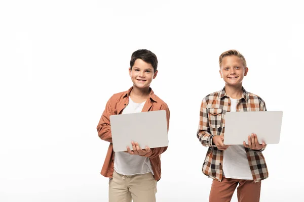 Два улыбающихся брата, держащих ноутбуки и улыбающихся в камеру, изолированные на белом — стоковое фото