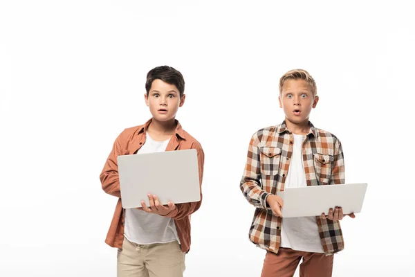 Два удивлённых брата держат ноутбуки и смотрят на камеру, изолированную на белом — стоковое фото