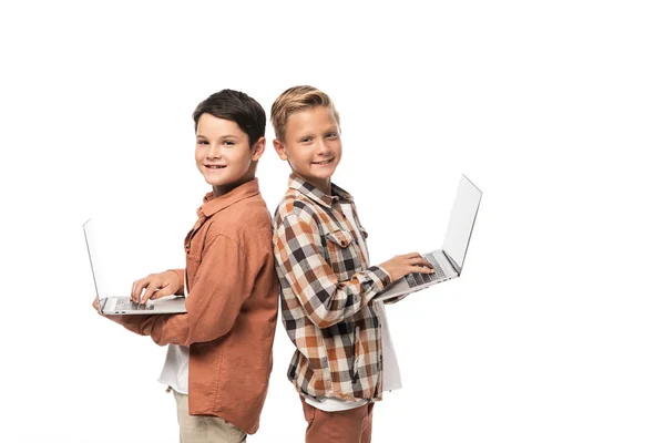 Dos hermanos alegres sosteniendo computadoras portátiles y mirando a la cámara aislada en blanco - foto de stock