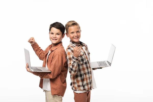 Dos hermanos sonrientes sosteniendo computadoras portátiles, mostrando los pulgares hacia arriba y mirando a la cámara aislada en blanco - foto de stock