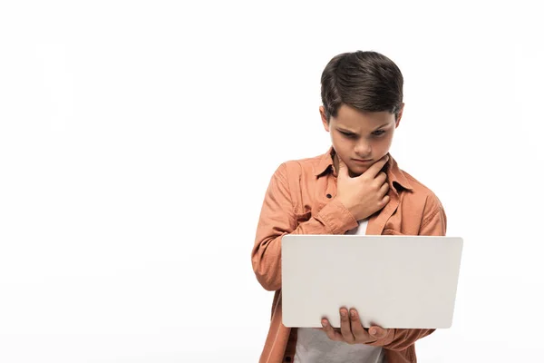 Ragazzo premuroso guardando il computer portatile e tenendo la mano vicino al viso isolato su bianco — Foto stock